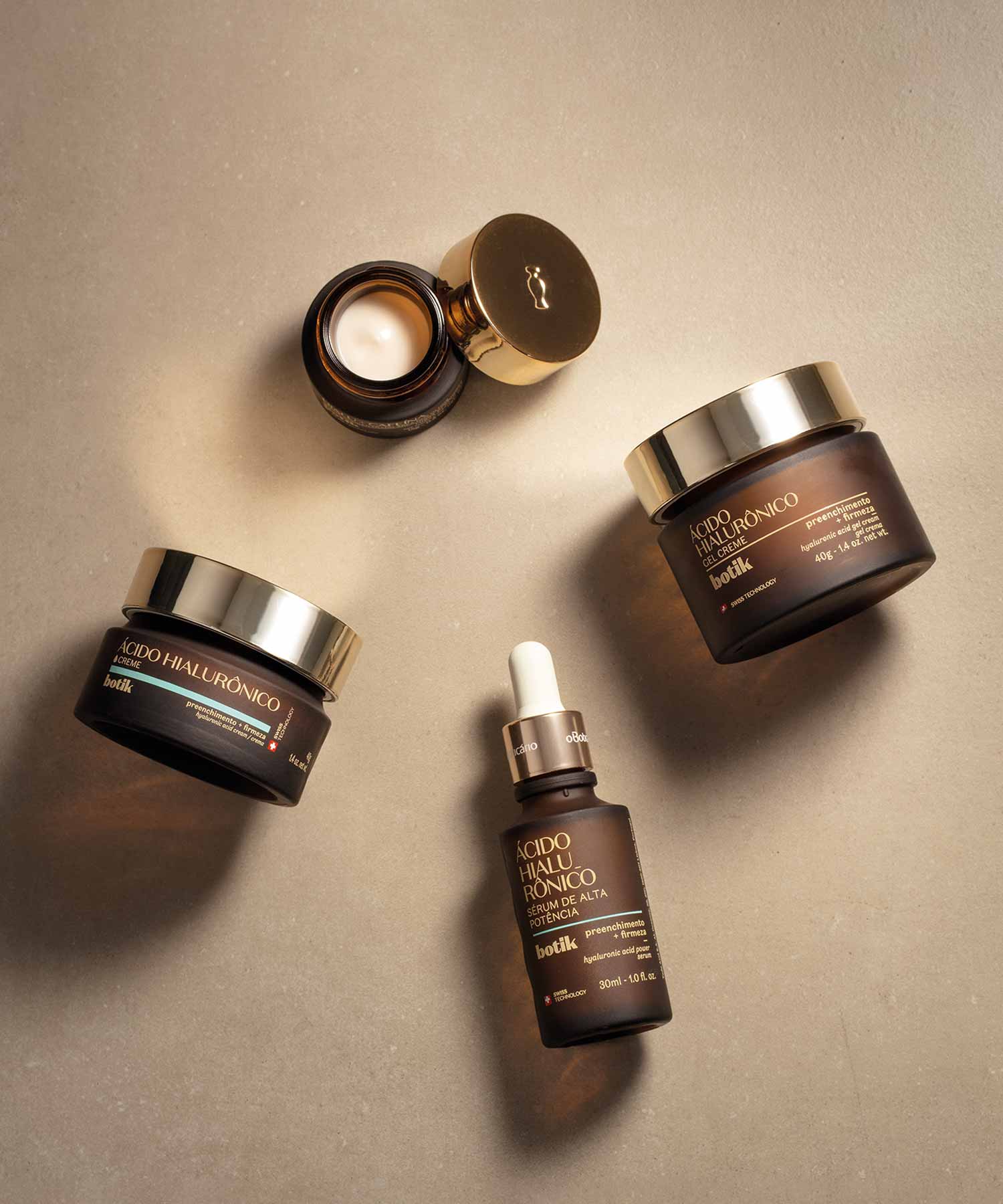 Quatro produtos da marca Botik, a marca de skincare do Boticário. Os produtos juntos completam uma rotina de cuidados faciais diária. Os produtos, em frascos castanhos, estão deitados num fundo creme e com as suas sombras visíveis, dando uma sensação de profundidade.
